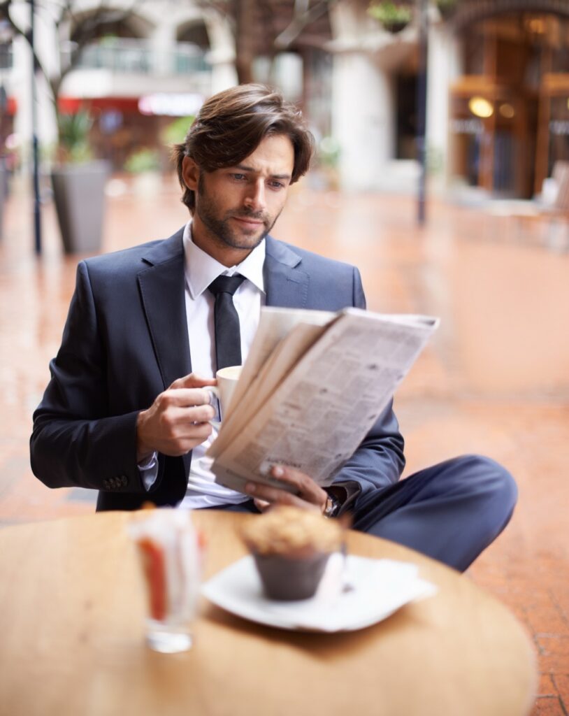 Corporate, man and reading newspaper at cafe with coffee, muffin and outdoor for information and updates. Businessman, cup and restaurant to search for business, opportunity and economy trends