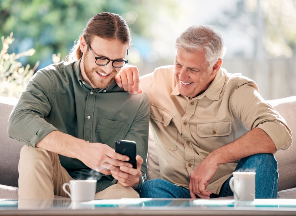 Senior, man and son with phone for browsing social media, streaming video and reading online news. Smile, people and mobile of communication, article and multimedia for bonding together at house